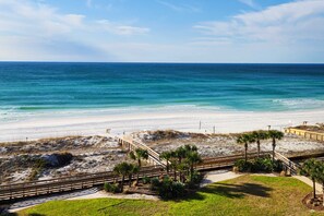 A beach with a wooden boardwalk, palm trees, and a view of the ocean. - Gulf-front condo with pool, hot tub & included beach service (Miramar Beach)