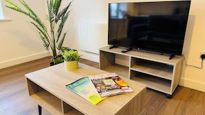 Una sala de estar moderna con una mesa de centro de madera, una revista, una planta en maceta y un televisor sobre un mueble.