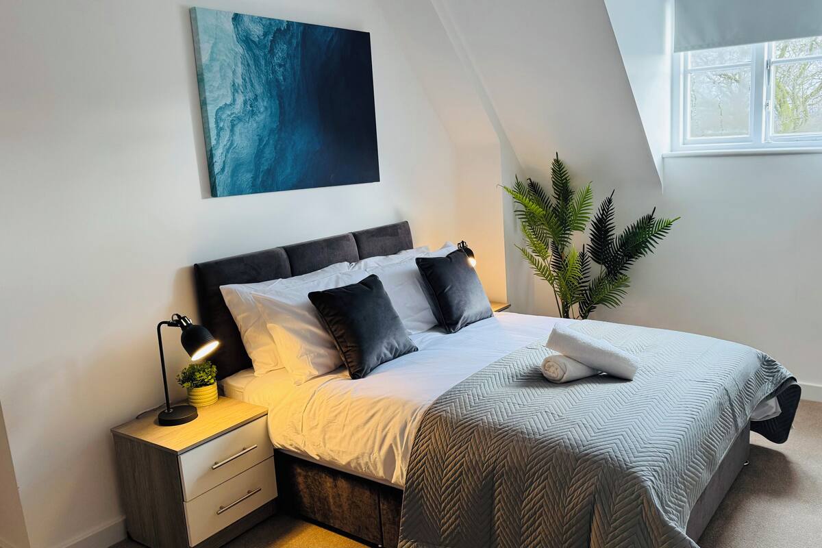 Une chambre à coucher avec un lit, une table de chevet, une lampe, une plante en pot et une fenêtre.