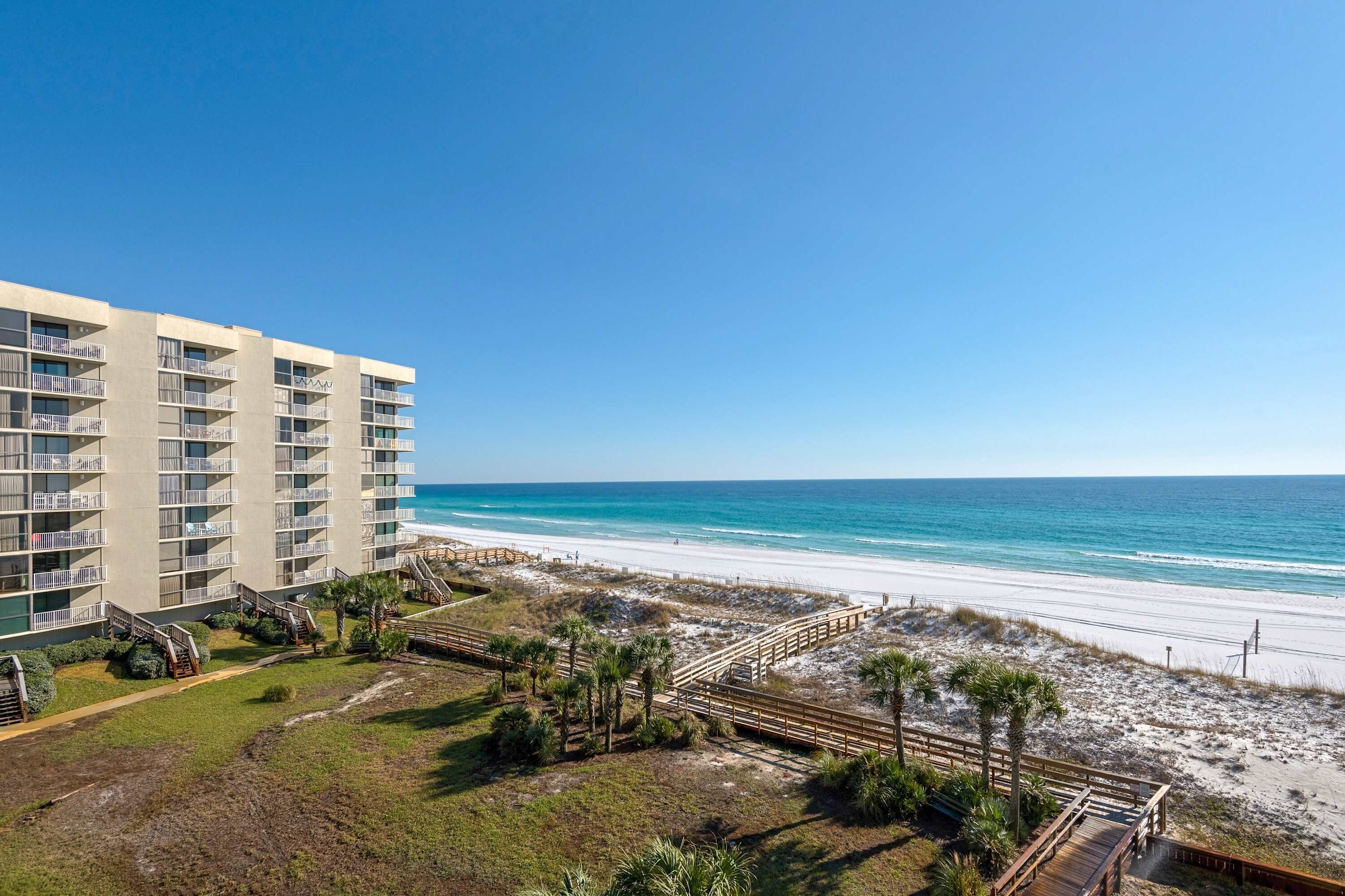 Ein Strandhotel mit mehreren Balkonen, einem Sandstrand und blauem Himmel.