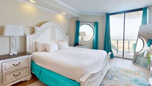 Habitación de hotel con una cama grande, una mesita de noche con lámpara, un aparador y vistas al exterior a través de un amplio ventanal.