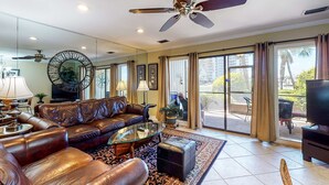 A spacious living room with a leather sofa, a glass coffee table, and a ceiling fan. - Cozy condo w/ a sunroom plus a shared pool & tennis - minutes from the beach (Miramar Beach)