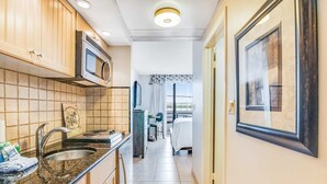 Una cocina pequeña con un fregadero, estufa y microondas. Un cuadro enmarco cuelga de la pared.