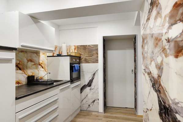 Une cuisine moderne avec des meubles blancs, un pare-feu en marbre et un plan de travail noir.