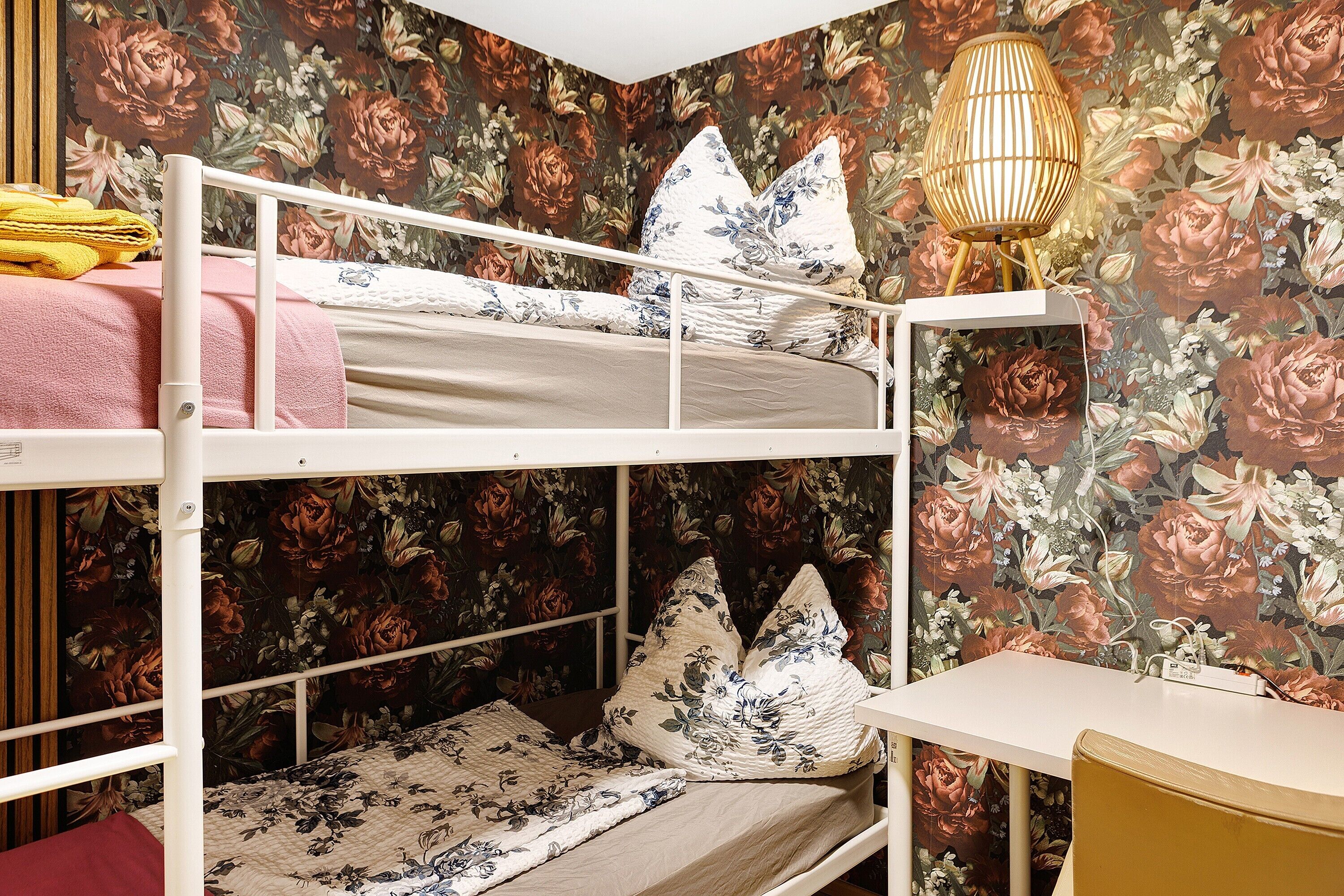 Ein Etagenbett mit Blumenmuster, ein Nachttisch mit Lampe und ein Sessel.