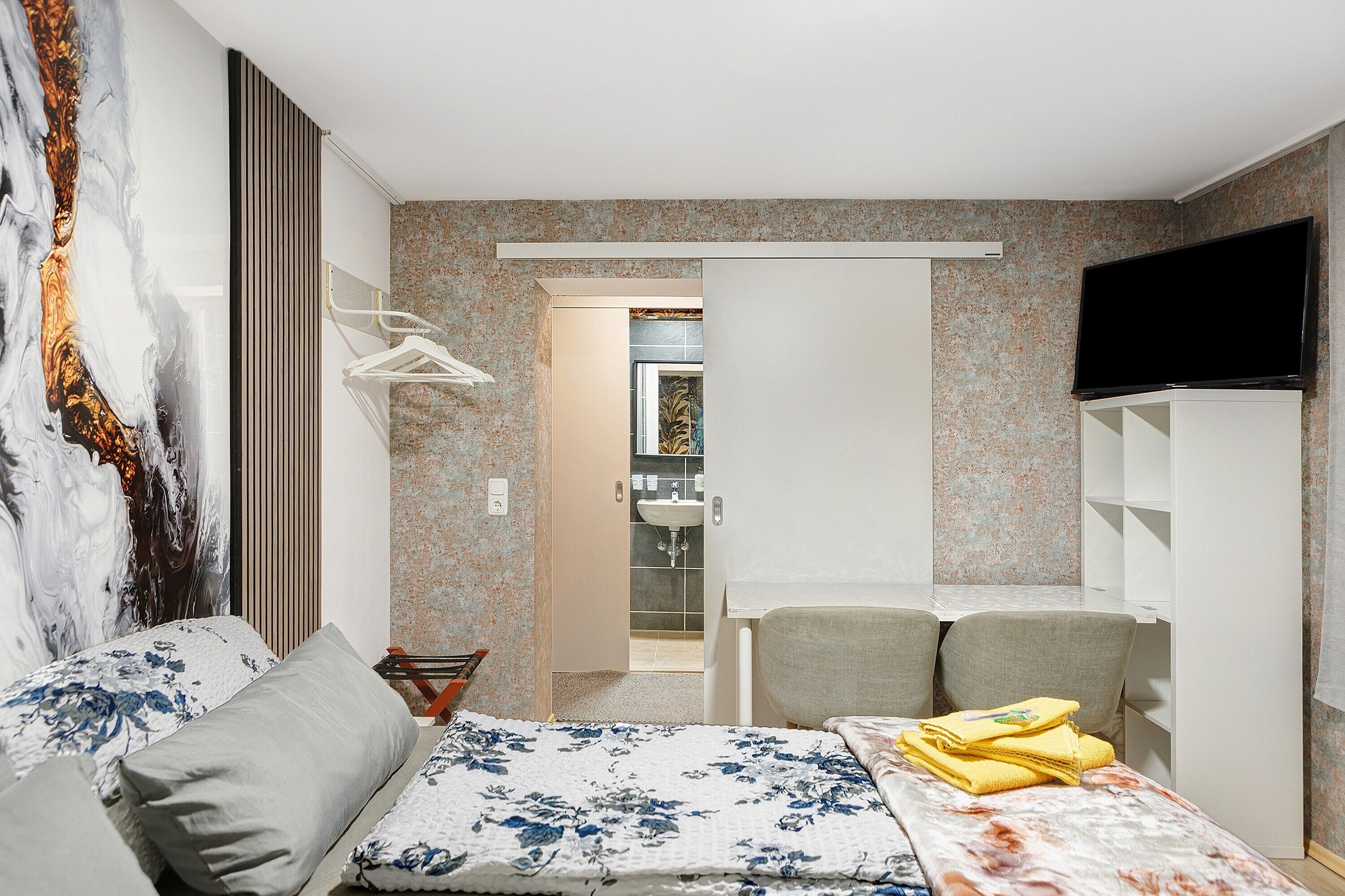 Une chambre à coucher avec un lit, une télévision, une armoire et une salle de bain visible à travers une porte ouverte.