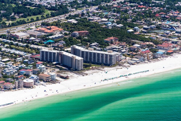 An aerial view of a coastal area with a beachfront hotel, a sandy beach, and a clear turquoise sea. - Mainsail End-Unit Townhome - Beachfront Resort, Pools, & Hot Tubs (Miramar Beach)