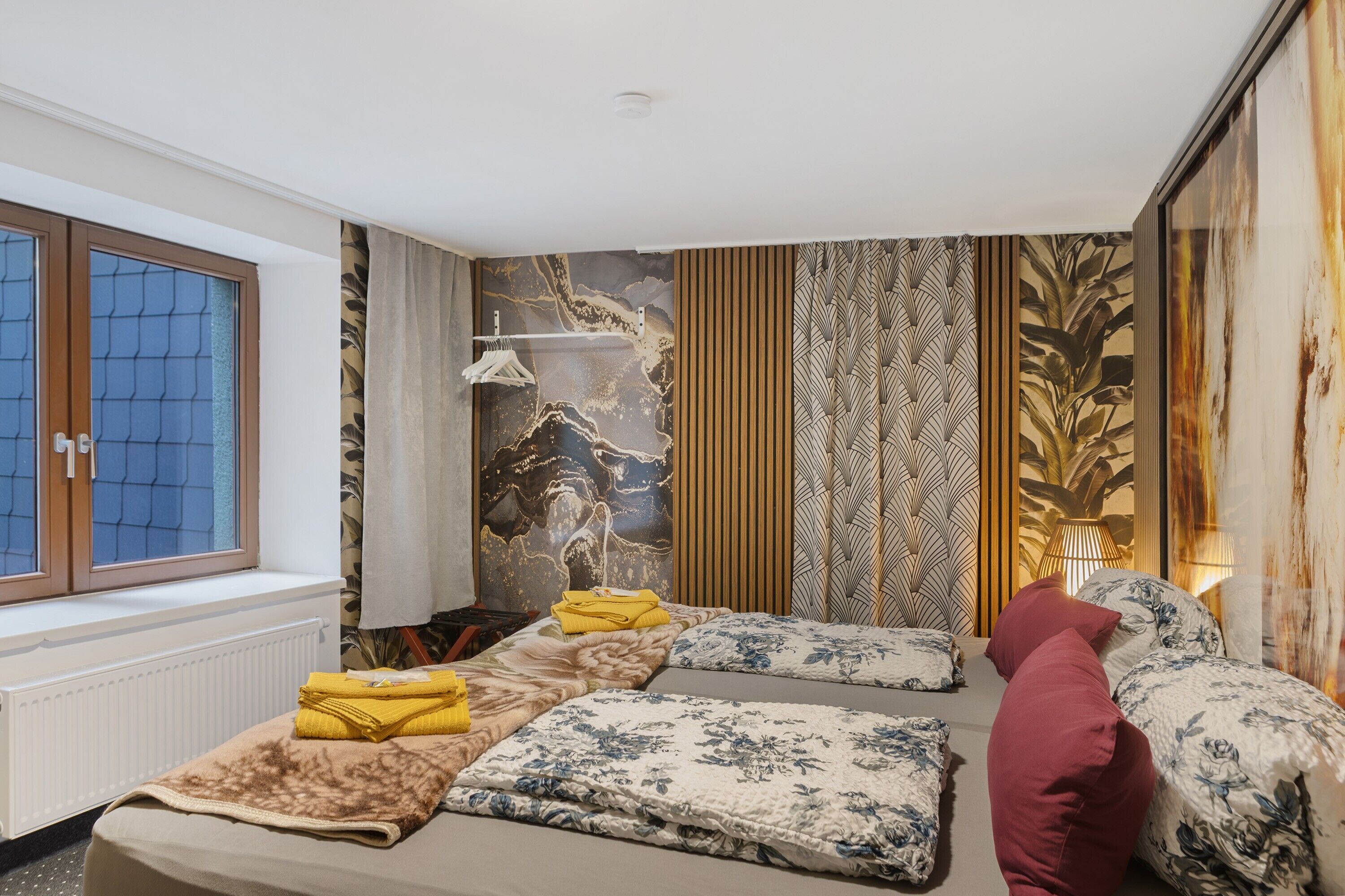 Camera da letto con due letti, una finestra, un termosifone e una parete con motivo decorativo.