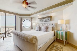 A spacious bedroom with a large bed, a ceiling fan, a nightstand, and a view of the outside. - Gulf view condo w/ balcony, shared pool/hot tub/tennis/gym & beach access (Miramar Beach)