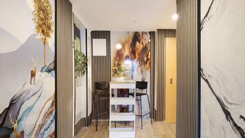 Ein modernes Interieur mit Holzboden, einem weißen Regalsystem, zwei schwarzen Stühlen und einer Wand mit einem Wandgemälde zum Thema Natur.
