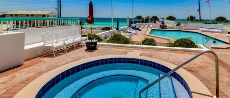 A pool area with a hot tub, lounge chairs, and a view of the ocean.