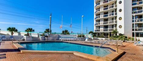 A swimming pool area with lounge chairs and a building with balconies in the background.