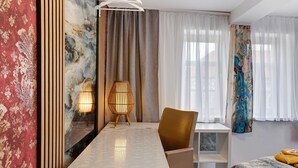 Ein modernes Hotelzimmer mit einem Tisch mit Marmorplatte, einem braunen Ledersessel, einem weißen Nachttisch und einem Bett mit einer strukturierten Decke.