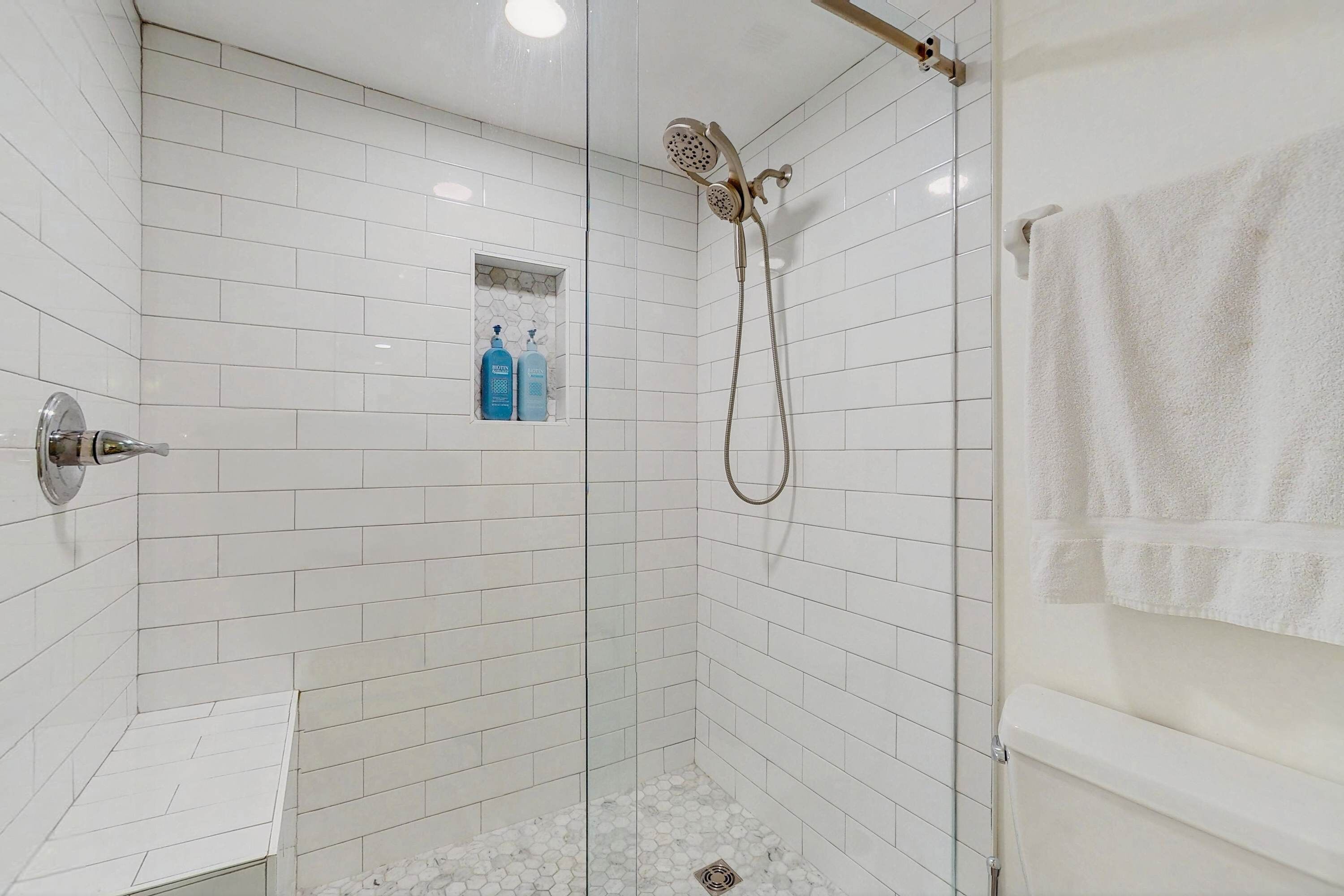 A modern shower area with white tiled walls, a glass door, and a towel rack.