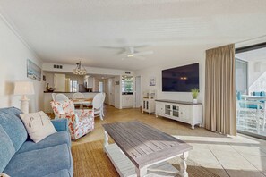 Ein geräumiges Wohnzimmer mit einem blauen Sofa, einem Holztisch und einem Essbereich mit weißen Stühlen.