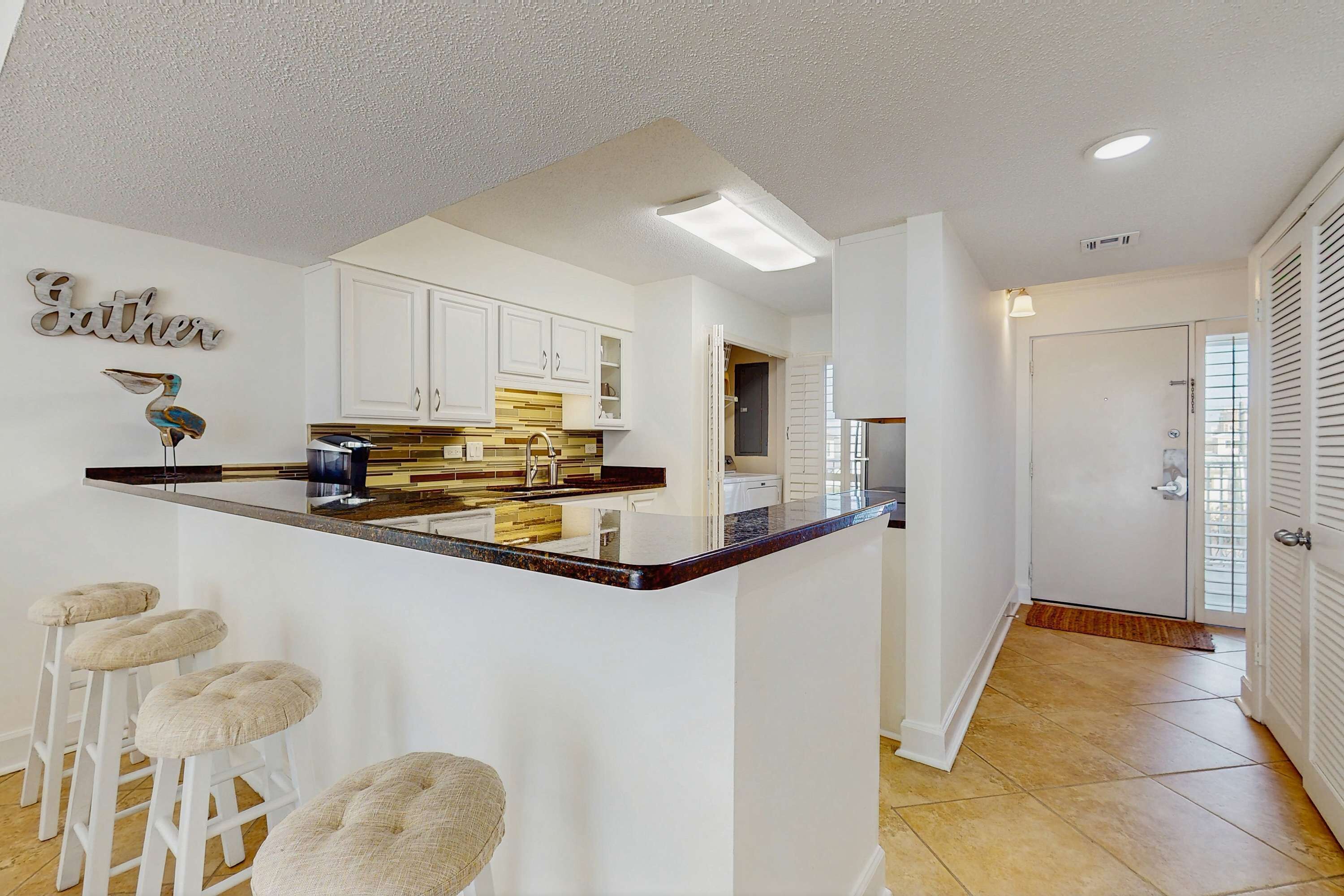 A modern kitchen with white cabinetry, a central island with stools, and a decorative wall piece.
