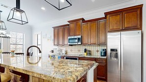 A modern kitchen with granite countertops, stainless steel appliances, and wooden cabinets. - Villa Lago - Tuscany Time (Miramar Beach)