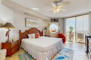 A bedroom with a large bed, a ceiling fan, a window with a view, a red chair, and a wooden nightstand. - Gorgeous waterfront retreat with tennis, basketball, pool, & hot tub (Miramar Beach)