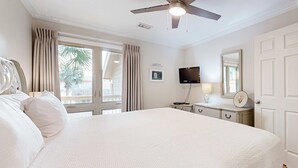 Ein Hotelzimmer mit einem großen Bett, einem Deckenventilator, einem Fernseher, einem Schreibtisch mit Lampe und einer Tür.
