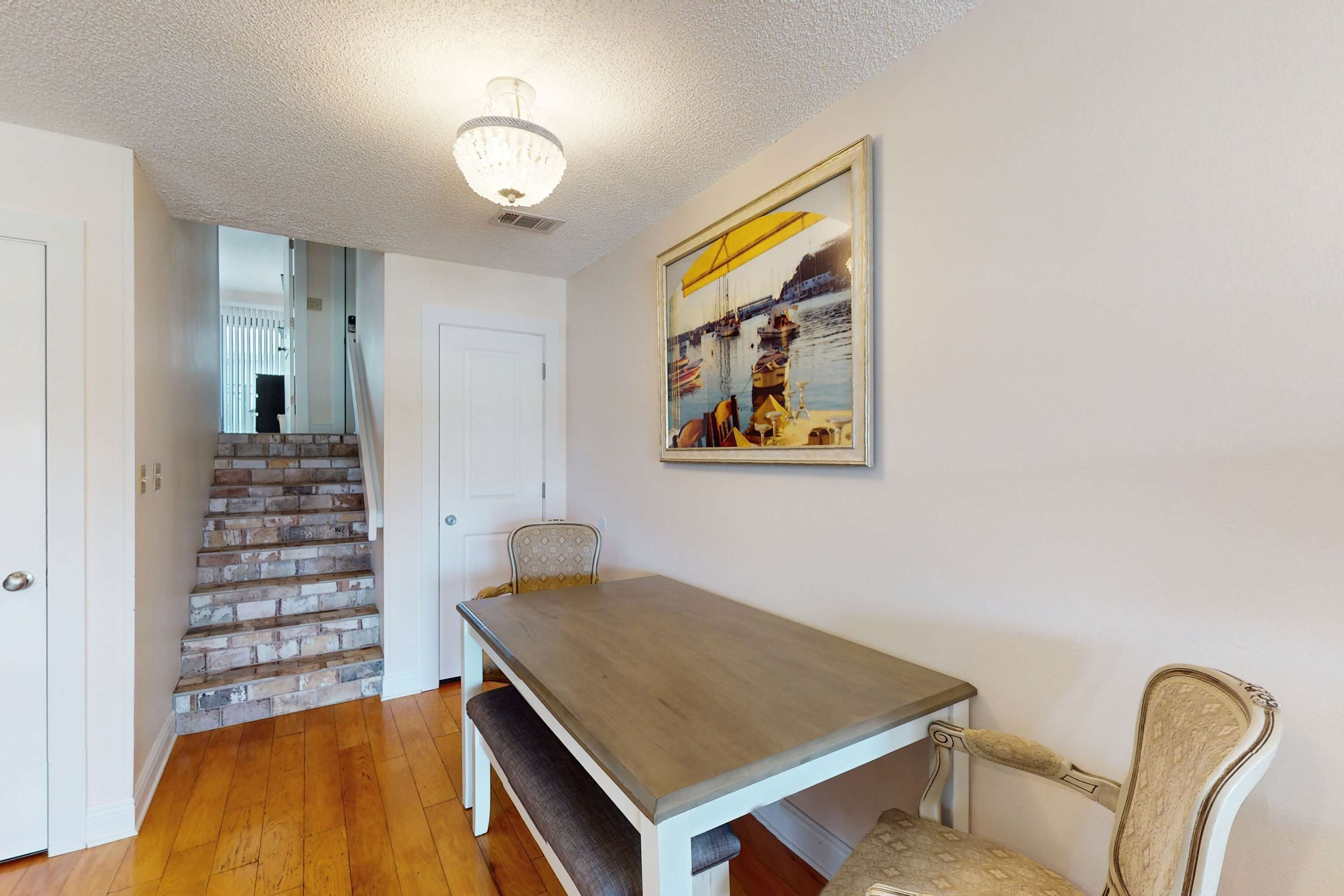 Un comedor con una mesa y sillas de madera, una escalera y un cuadro en la pared.