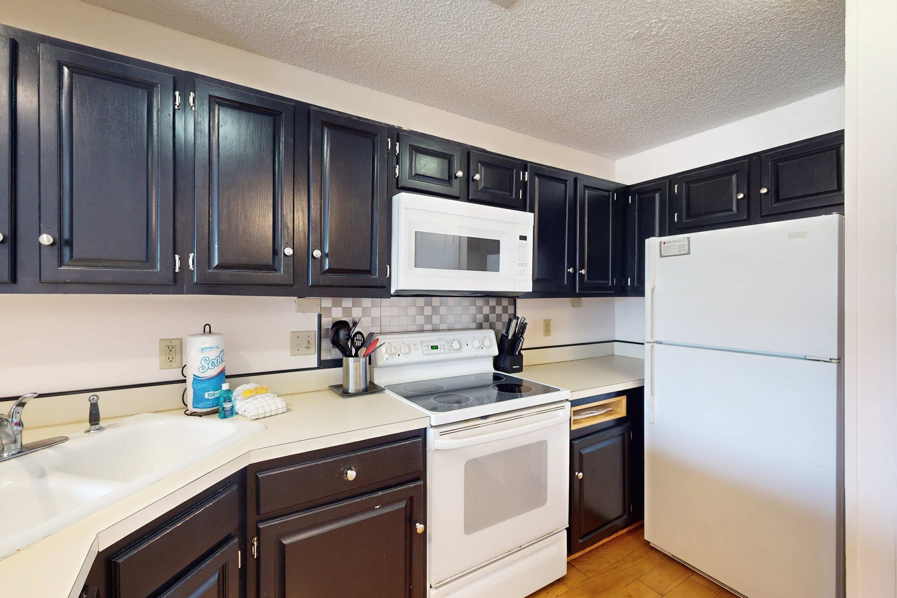 A kitchen with dark cabinets, a white microwave, a stove, and a refrigerator.