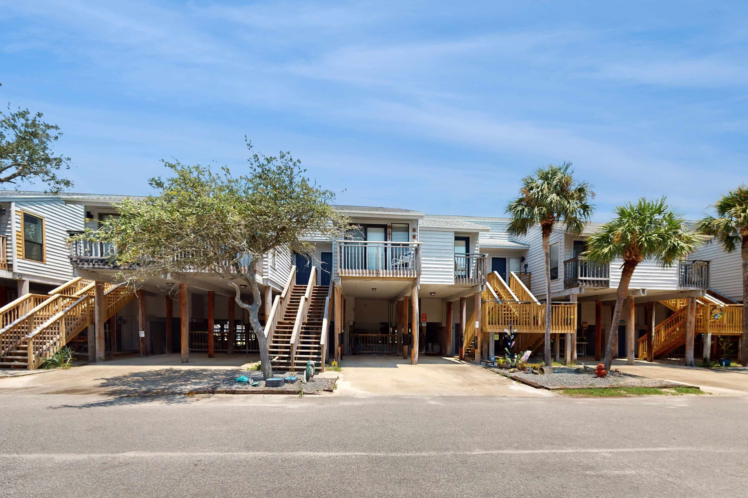 A row of beachfront condominiums with balconies, wooden staircases, and palm trees.