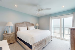 A bedroom with a large bed, two bedside lamps, a ceiling fan, and a view of the balcony. - Spacious & updated waterfront home w decks, beach views & private boardwalk (Cape San Blas)