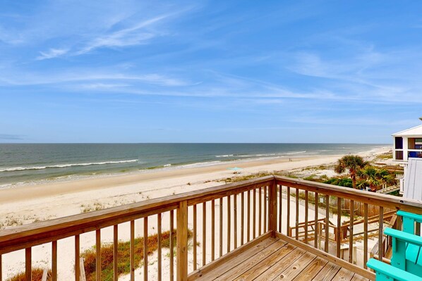 Une terrasse en bois offrant une vue sur une plage de sable et l’océan.