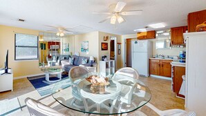A spacious living area with a glass dining table, a ceiling fan, and a kitchen with wooden cabinets.