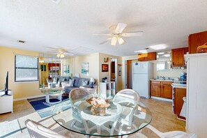 A spacious living area with a glass dining table, a ceiling fan, and a kitchen with wooden cabinets.