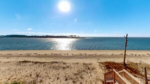 A beach with a wooden staircase leading down to the sand, a clear sky, and calm water.