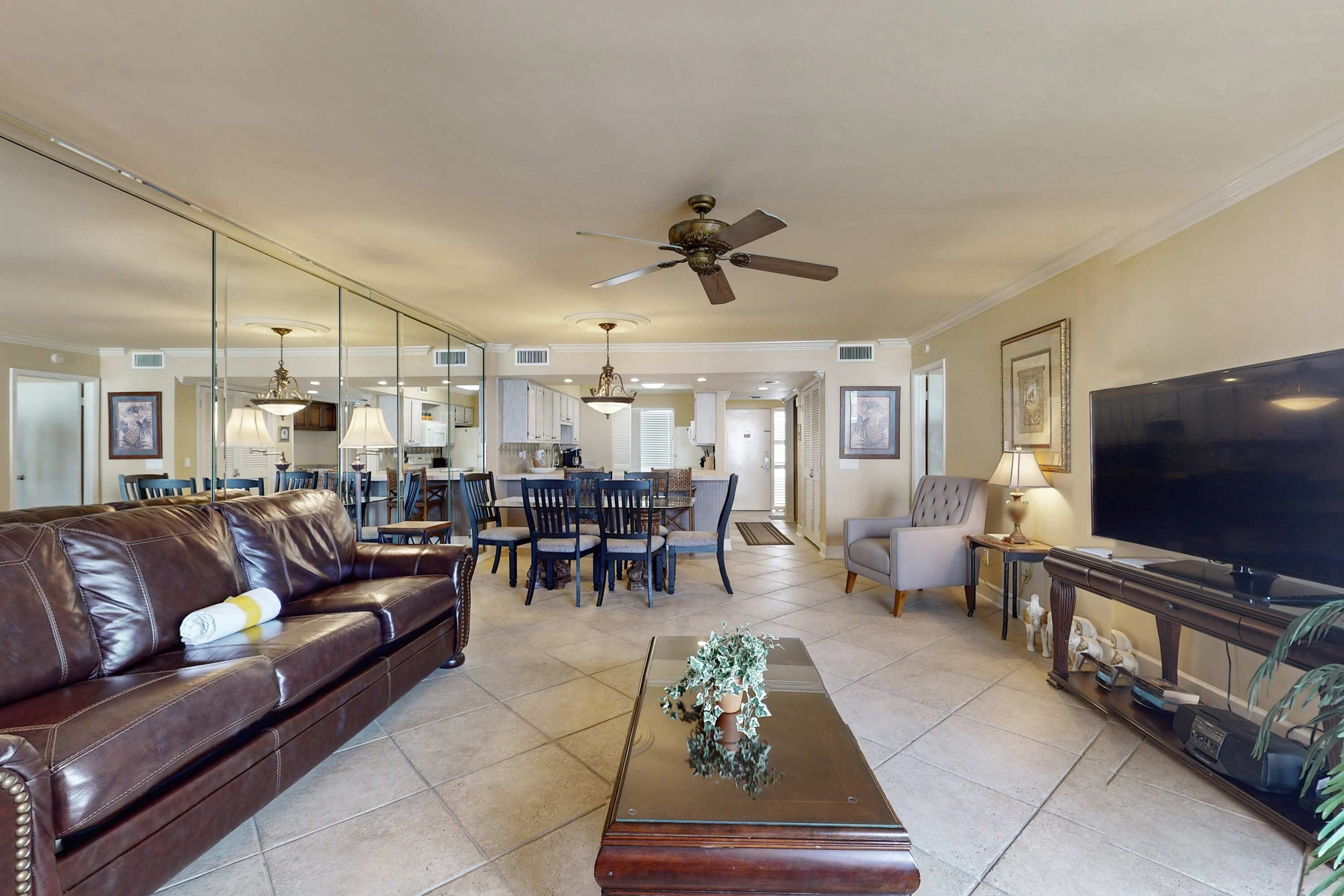A spacious living room with a leather sofa, a coffee table, a TV, and a dining area in the background.