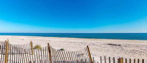 A beach with a wooden fence in the foreground and a clear blue sky.