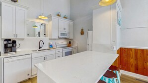 Una cocina moderna con armarios blancos, una isla central y detalles de madera en las paredes.