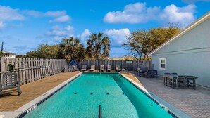 Una piscina rectangular con un deck de madera y sillas de descanso.