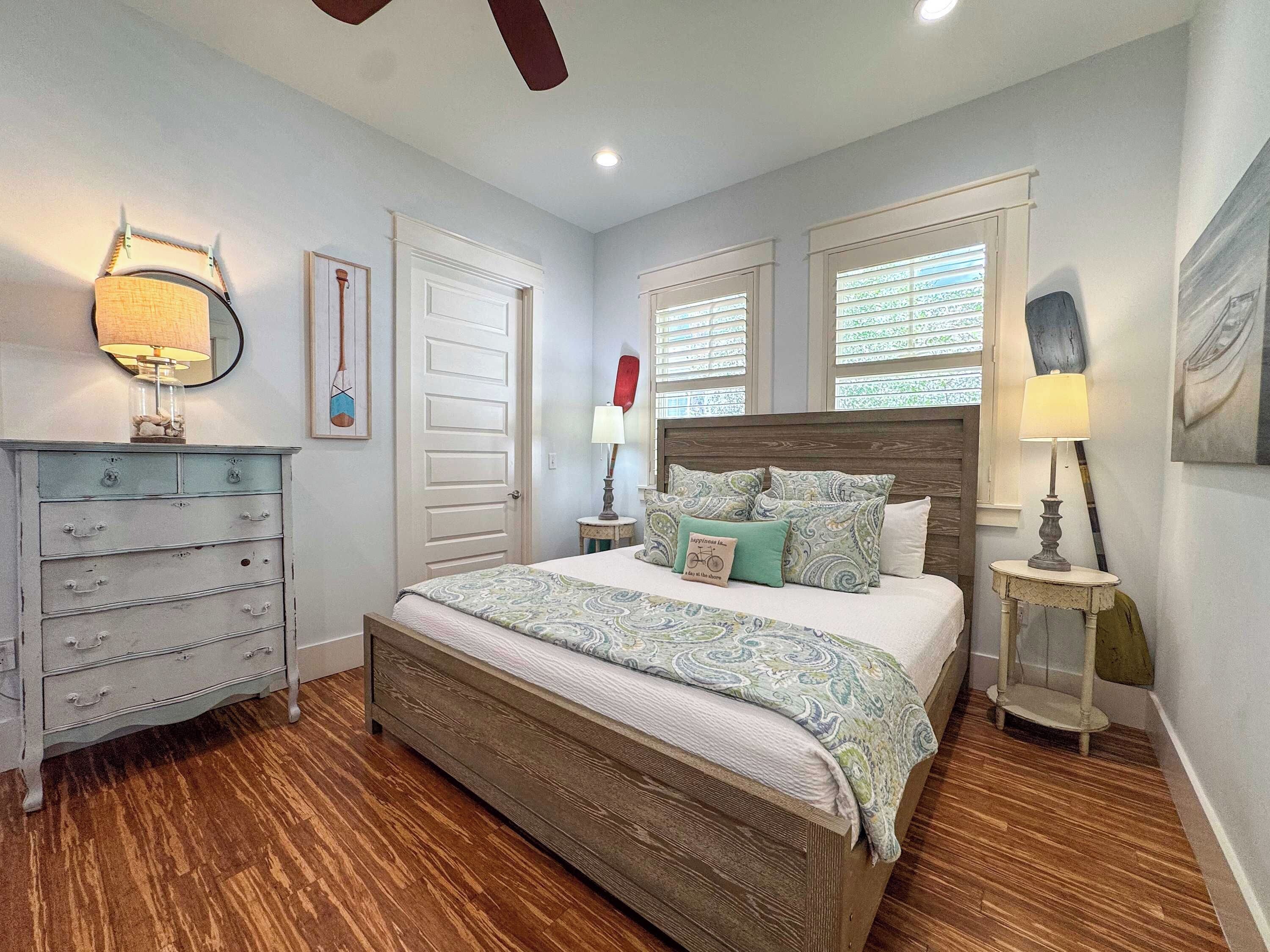 Une chambre à coucher avec un lit en bois, une commode, une table de chevet, une lampe et une fenêtre avec des stores.