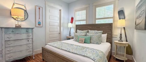 Un dormitorio con cama de madera, cómoda, mesita de noche, lámpara y ventana con persianas.