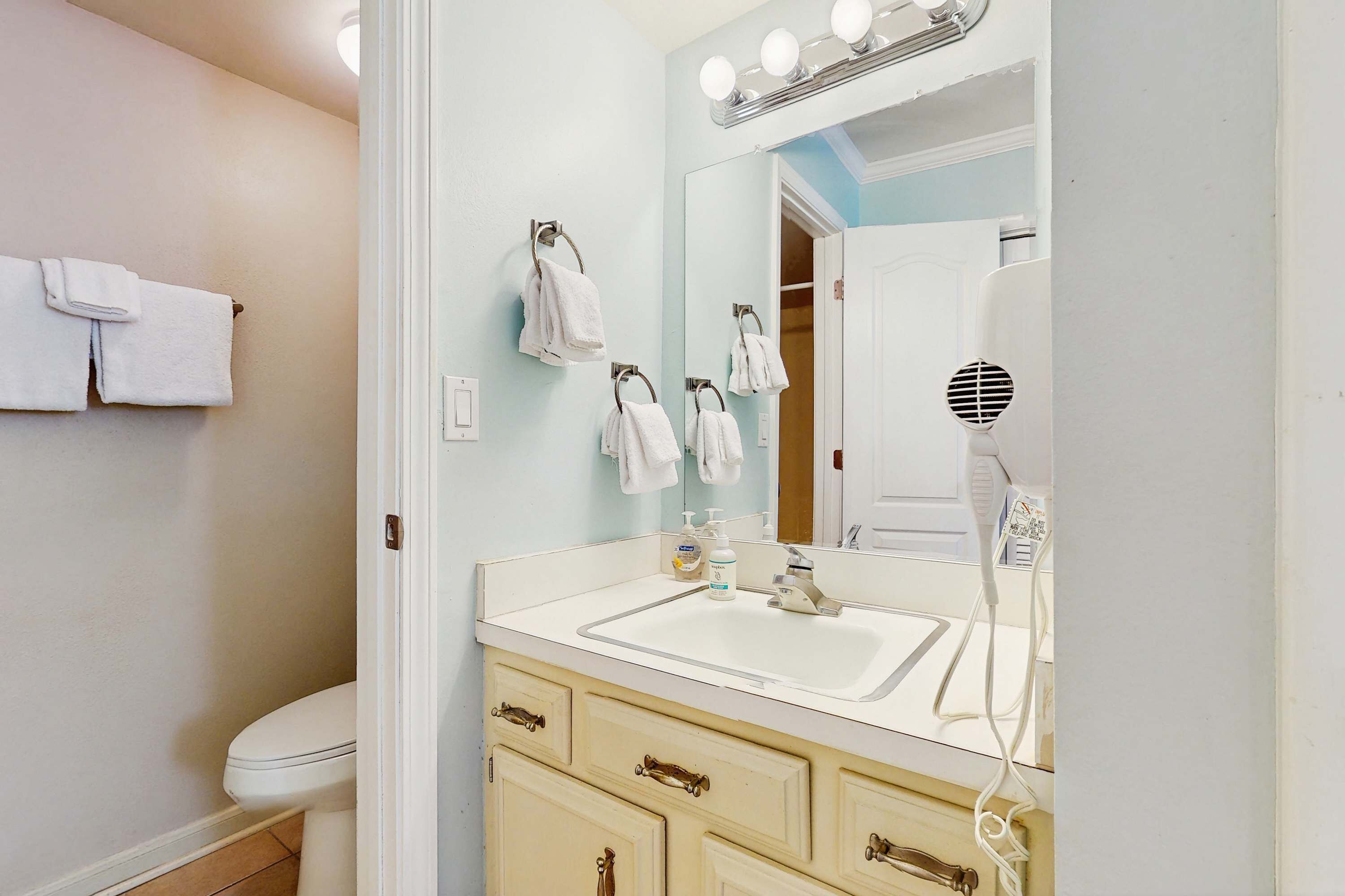 A bathroom with a white sink, a mirror with lights, and a towel rack.