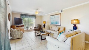 Sala de estar com sofá, poltrona, mesa de centro, televisão e luminárias.