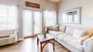 A living room with a beige sofa, a wooden coffee table, and a large mirror on the wall. - Cozy Hotel-Style- near beach & dining with kitchenette, pools, hot tub, & tennis (Santa Rosa Beach)