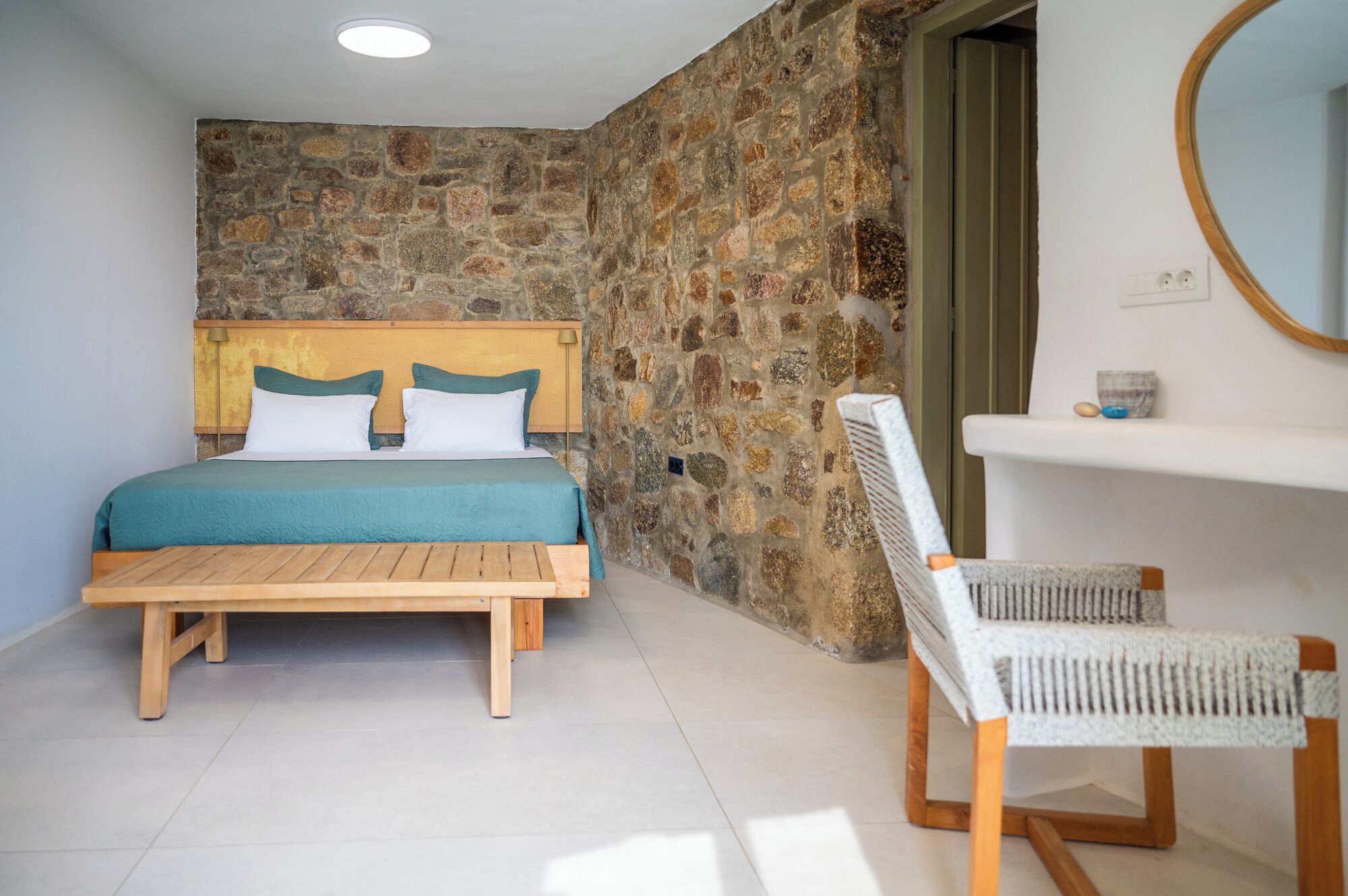 Camera da letto con parete in pietra, un letto di legno, una sedia e un piccolo bagno.