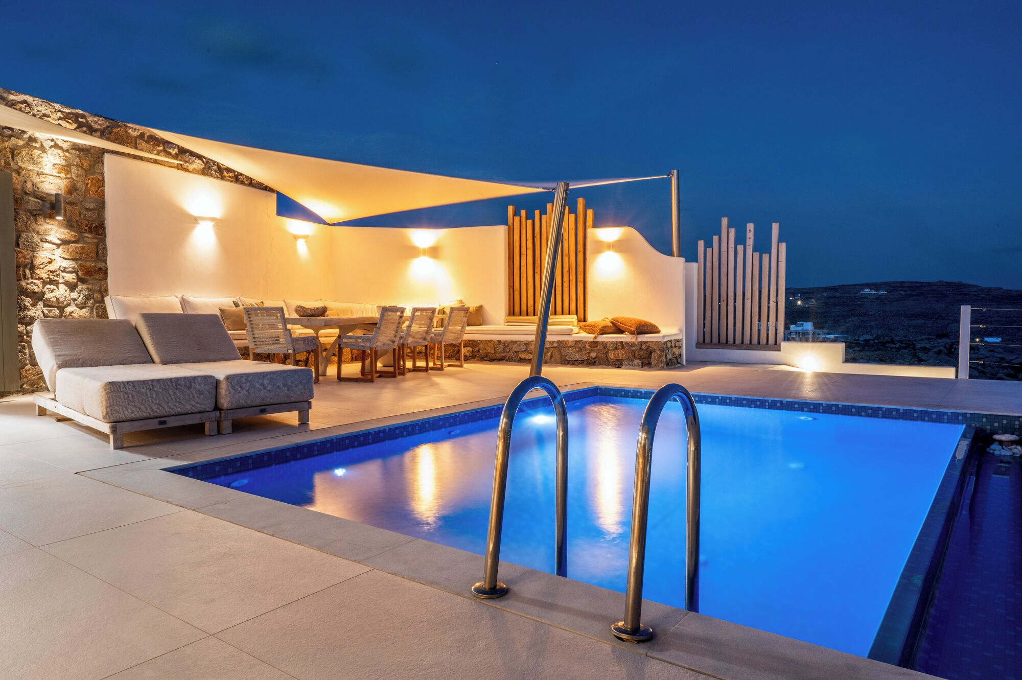 A modern outdoor pool area with a stone wall, lounge chairs, and a dining table.