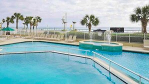 A swimming pool with a curved design, surrounded by a white fence and palm trees. - Majestic Sun A806 Beachfront Views & Pool Fun! (Miramar Beach)