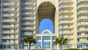 A high-rise hotel with multiple balconies, a central archway, and palm trees in the foreground. - Majestic Sun A806 Beachfront Views & Pool Fun! (Miramar Beach)