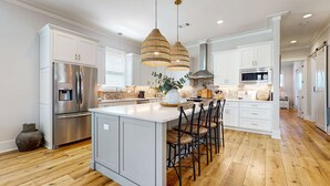 A modern kitchen with white cabinetry, stainless steel appliances, a central island with bar stools, and pendant lighting. - Gorgeous coastal home with shared pools, golf cart, and beach access (Miramar Beach)