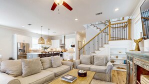 A spacious living room with a sofa set, a coffee table with a book, and a staircase with a railing. - Gorgeous coastal home with shared pools, golf cart, and beach access (Miramar Beach)