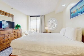 A hotel room with a large bed, a wooden dresser, a television, and a view of the outdoors. - Resort condo with pool, hot tub & on-site dining, near the beach (Miramar Beach)