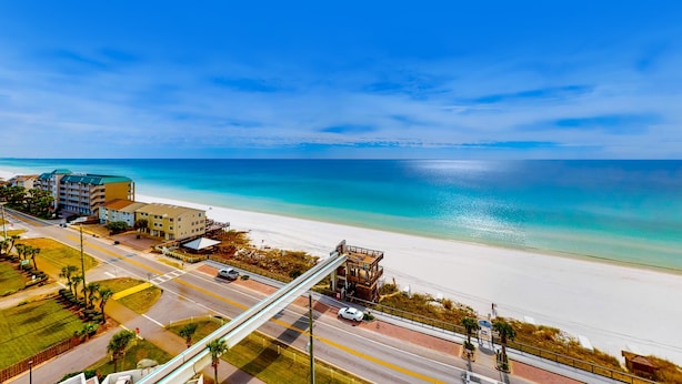 A coastal road with a pedestrian bridge, a beach, and buildings in the background. - Resort condo with pool, hot tub & on-site dining, near the beach (Miramar Beach)