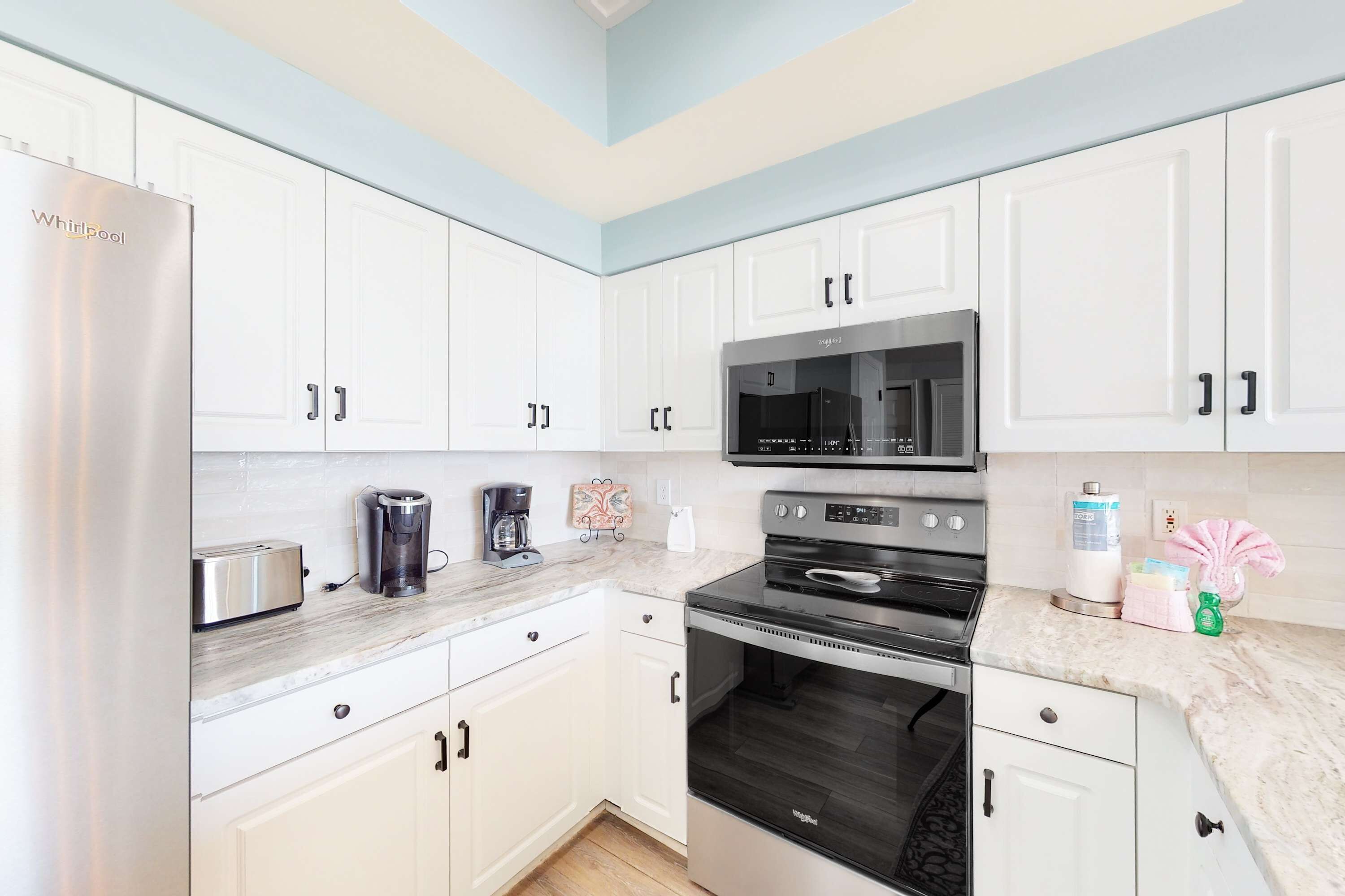 A modern kitchen with white cabinets, a stainless steel refrigerator, a microwave, an oven, and a marble countertop.
