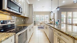 Una cocina moderna con electrodomésticos de acero inoxidable, encimeras de granito y abundante luz natural gracias a amplias ventanas.